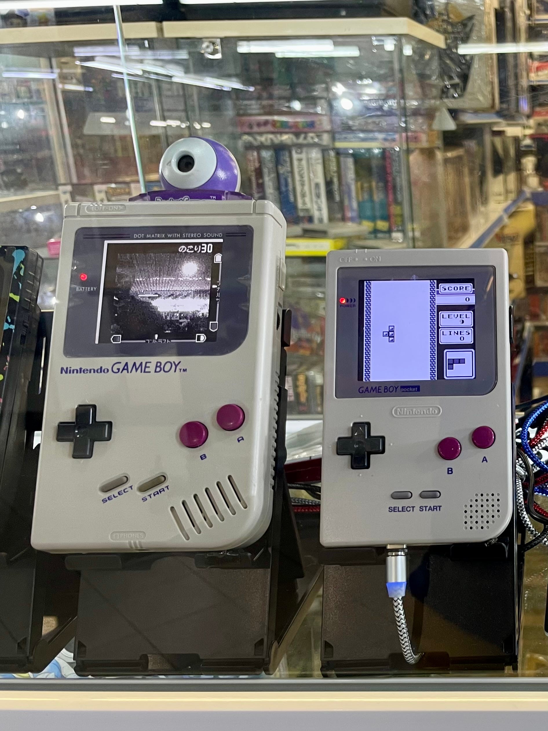 Two vintage handheld game consoles in a display case