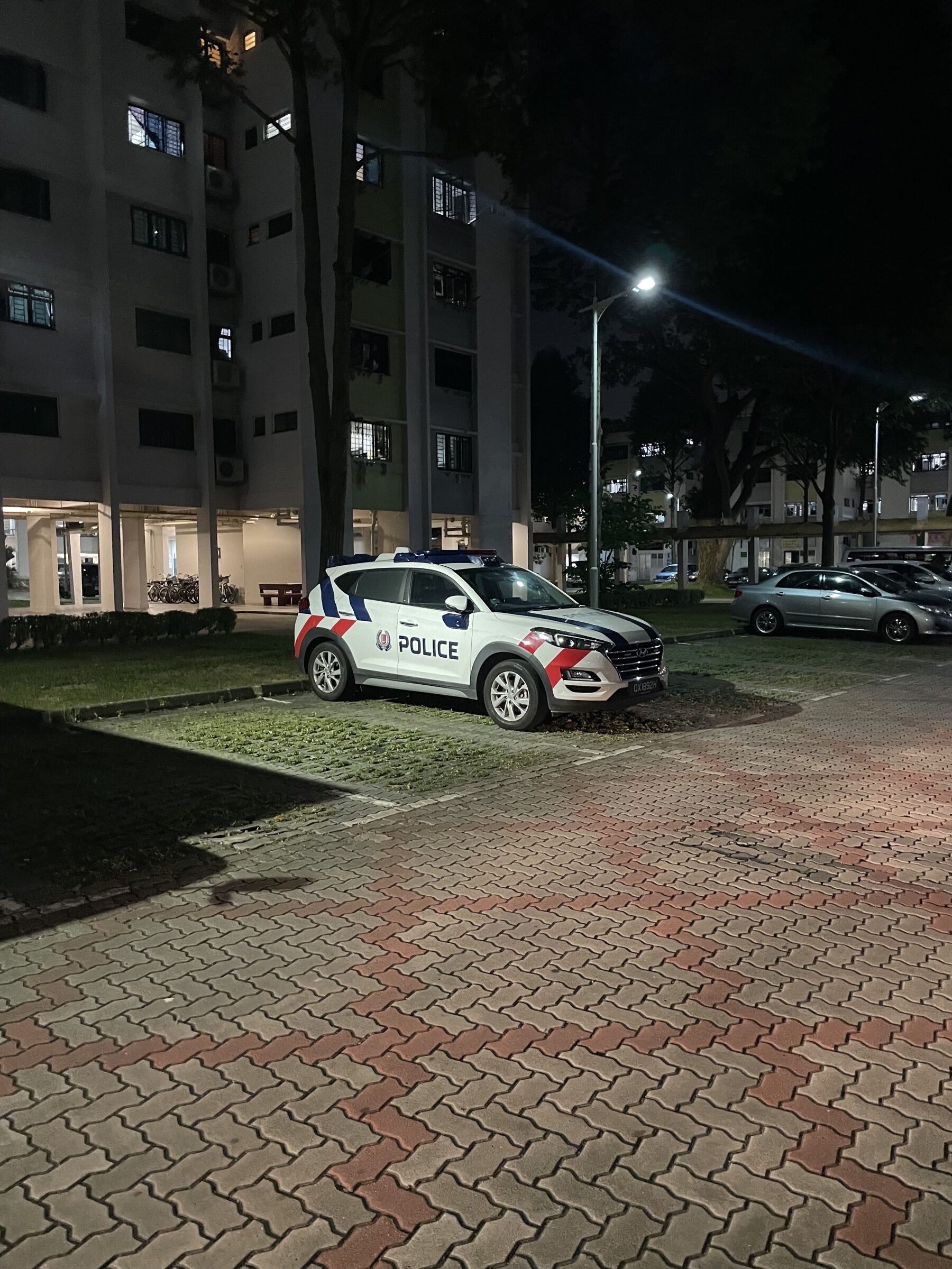 A Singapore police car parked outside residential blocks in Bedok at night.