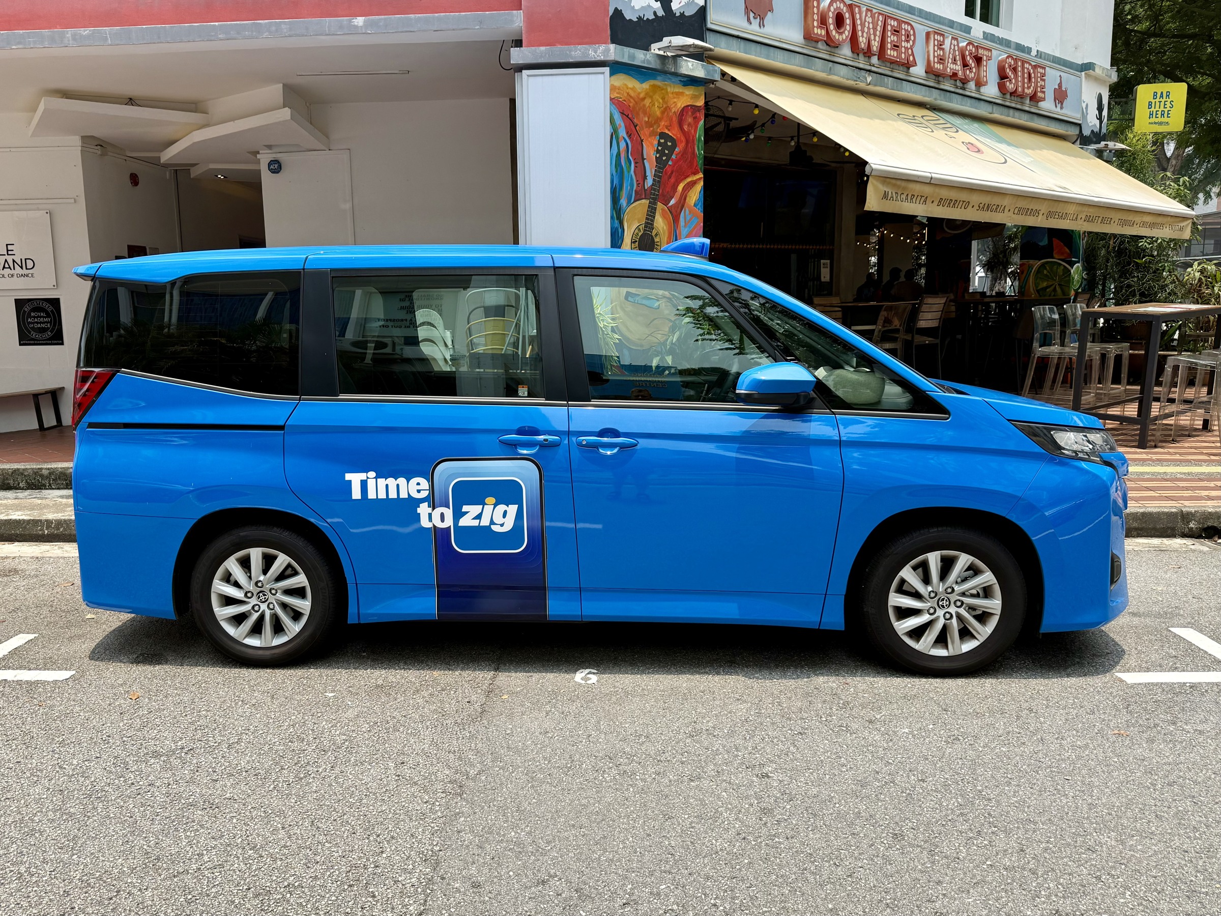 Blue Singapore taxi with a large “Time to zig” slogan on its sliding door.