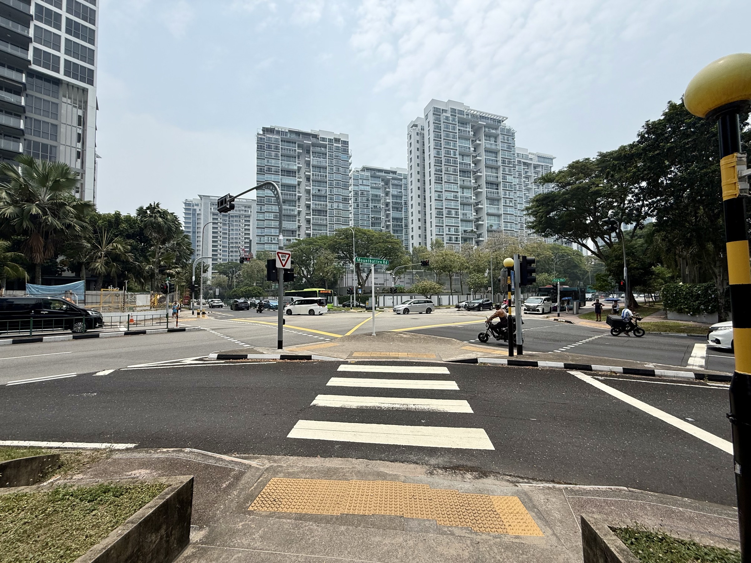 Pedestrian crossing and traffic island at the Katong junction, with a Mountbatten Road sign and residential towers beyond.