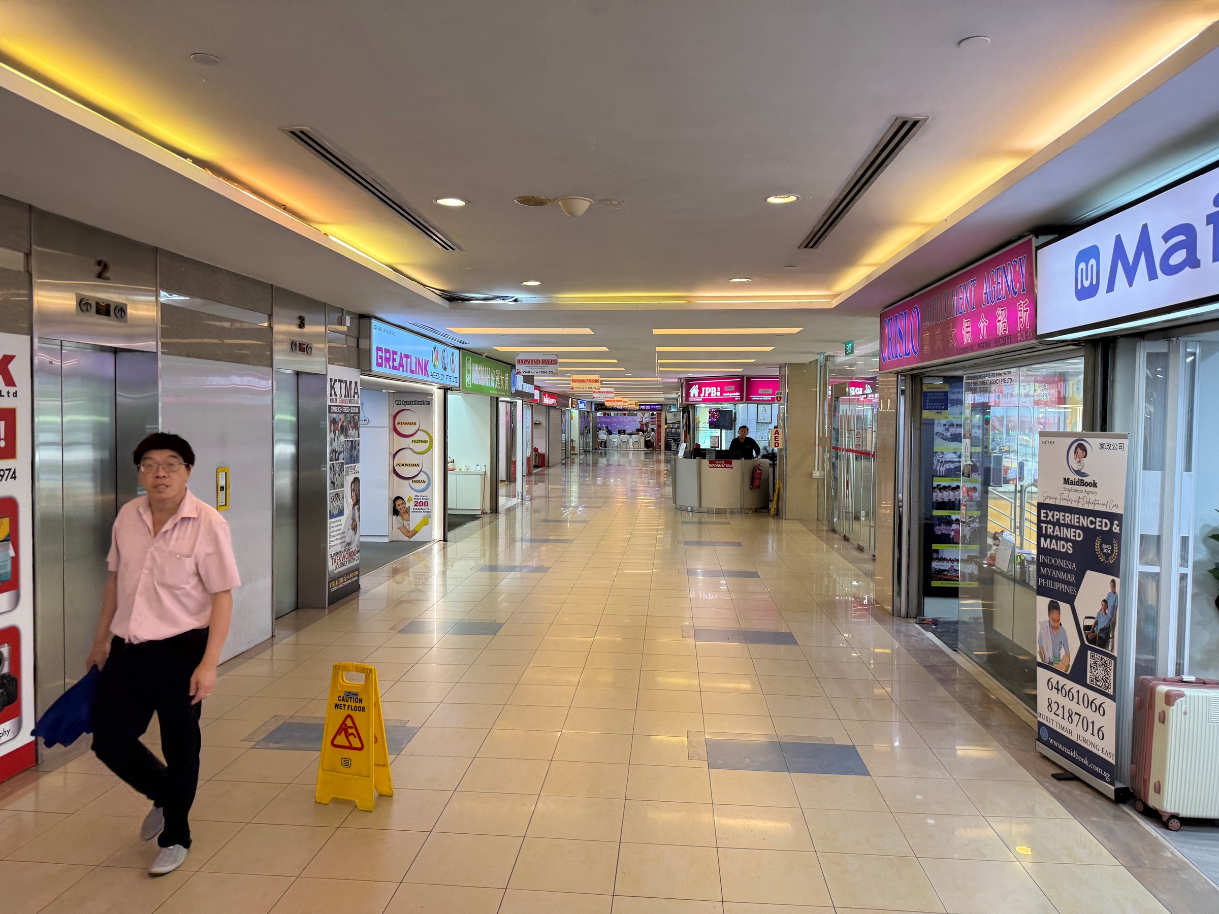 A long tiled corridor lined with employment agencies, with lifts on the left.