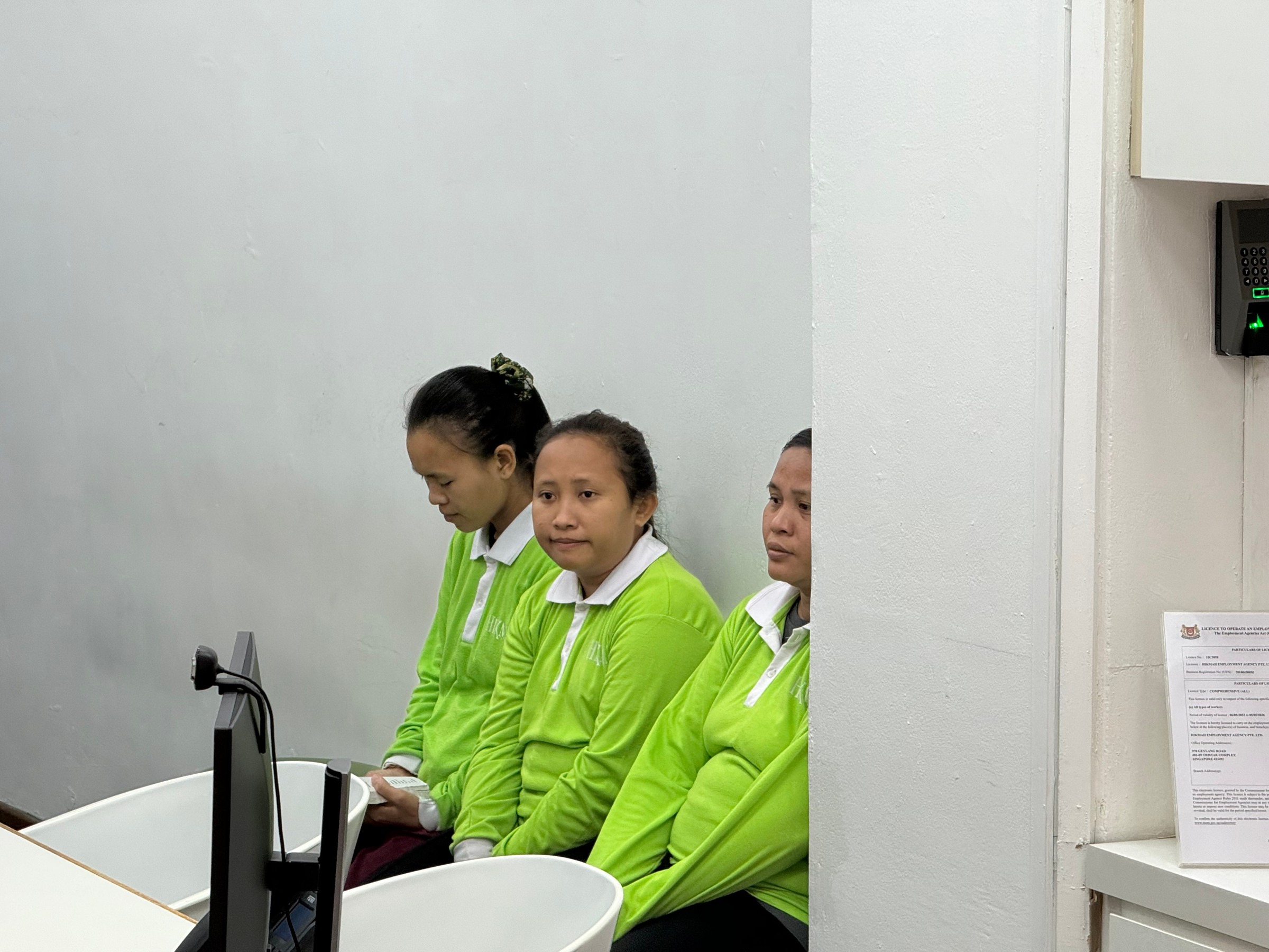 Women in green shirts seated in an employment agency, one looking towards the camera.