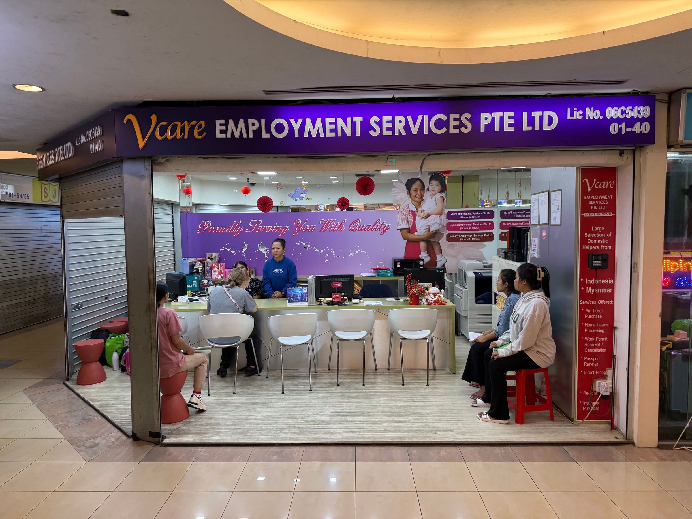 The purple Vcare sign above an employment agency with people seated beside the counter.