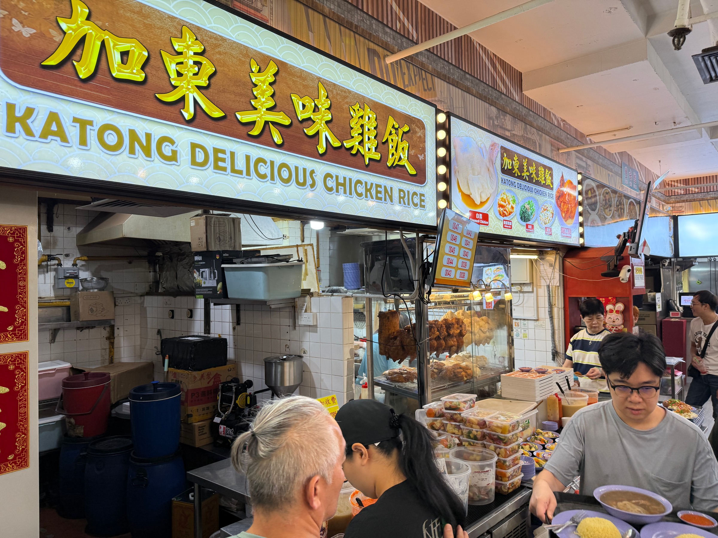 The Katong Delicious Chicken Rice sign above the counter and diners.