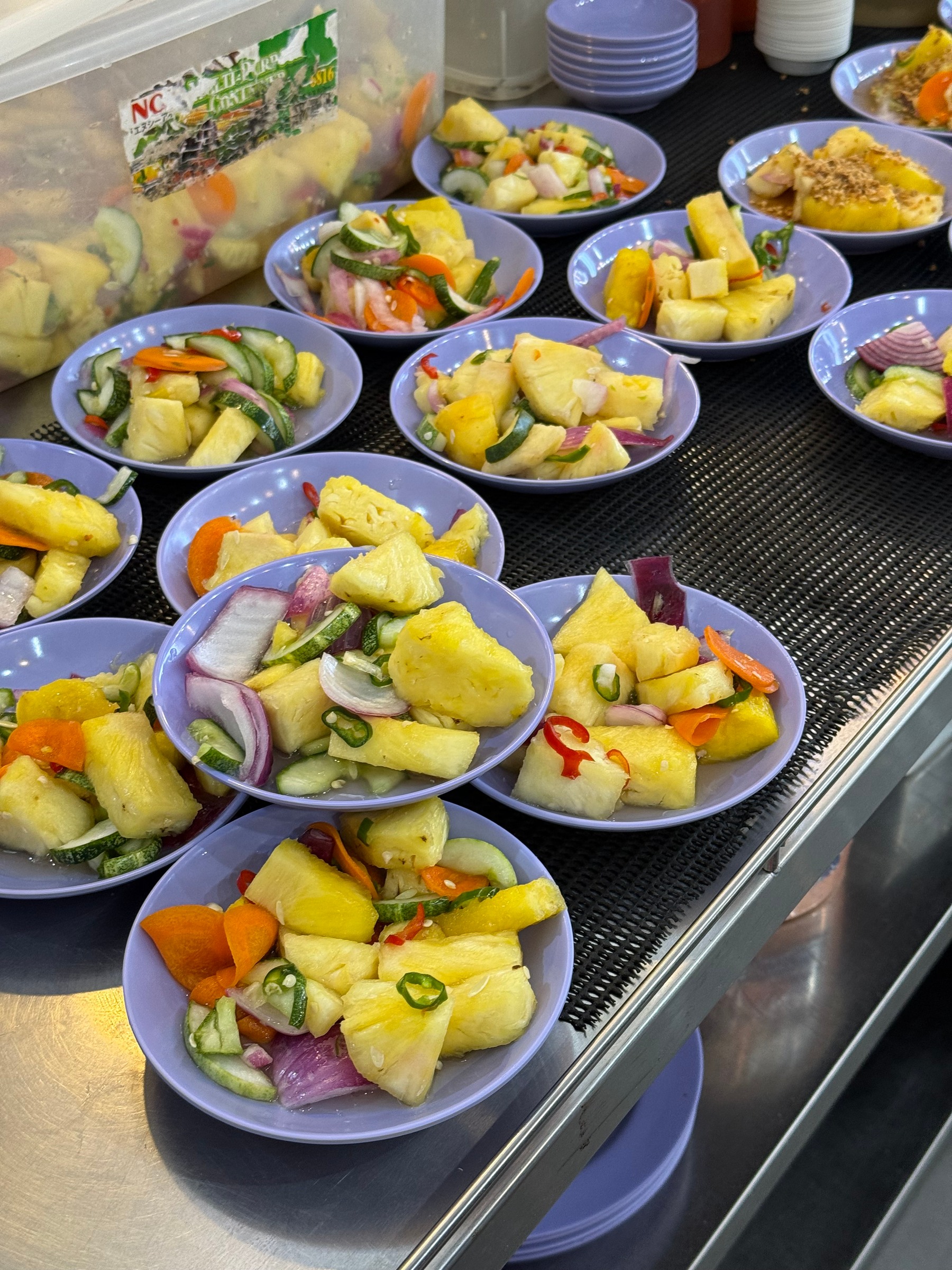 Rows of small plates holding pineapple, cucumber and other vegetables.