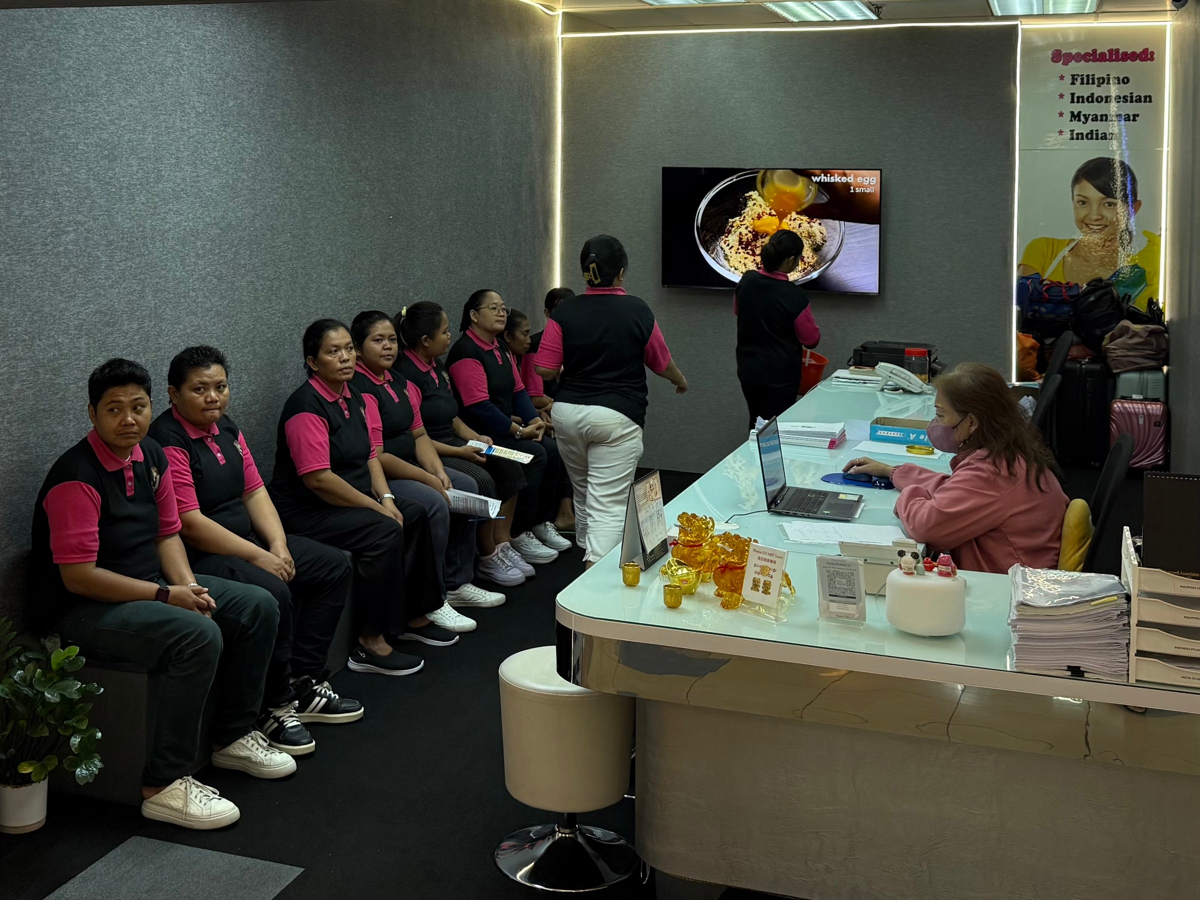 Women in matching pink-and-black shirts seated inside Great Employment agency.