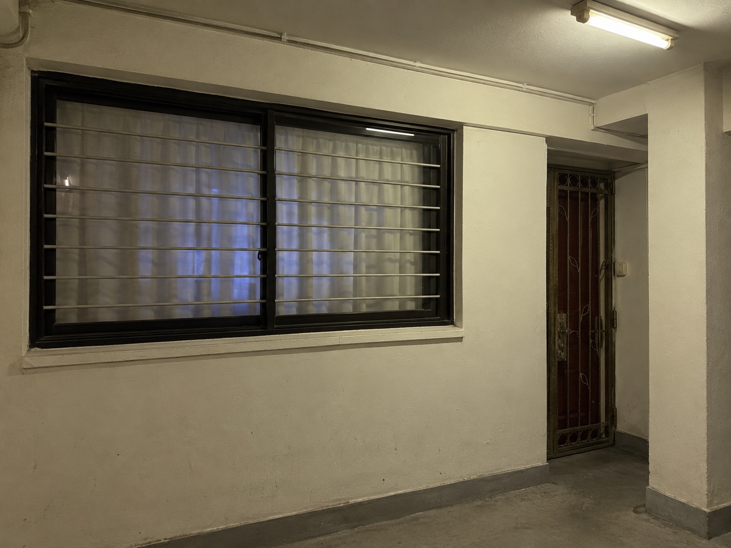 Curtained window and a recessed apartment entrance along an HDB corridor at night