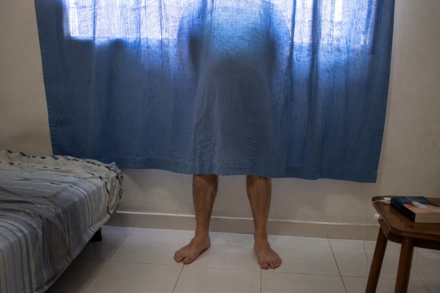 Bare lower legs visible below a blue curtain in a lived-in bedroom.