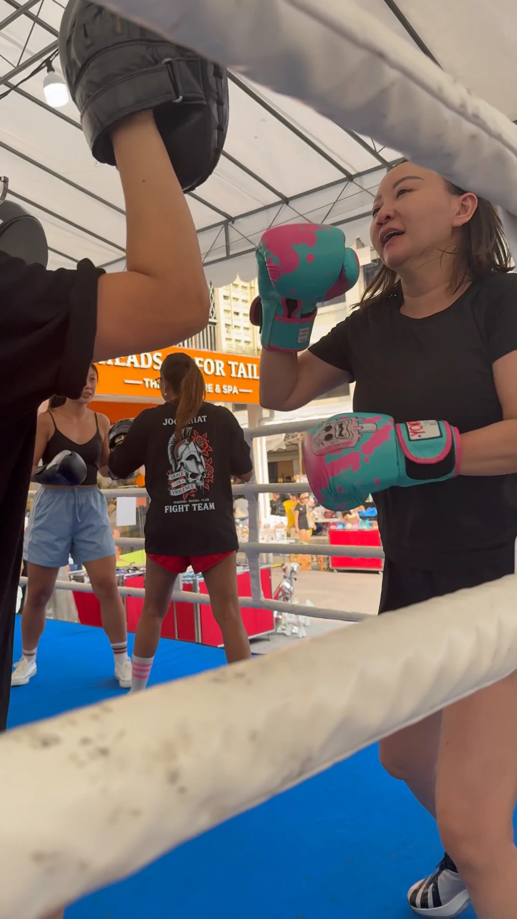 A participant practises punches with a trainer in an outdoor boxing ring.