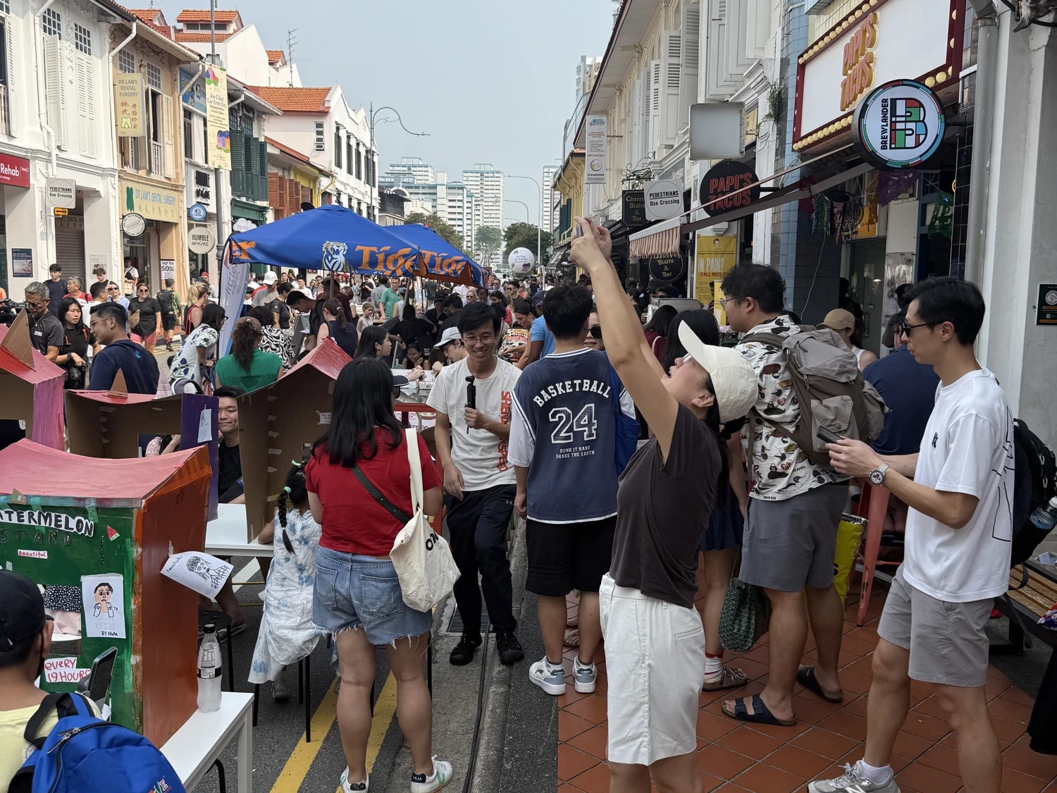 A crowd fills Joo Chiat Road beside street games and colourful shophouses.