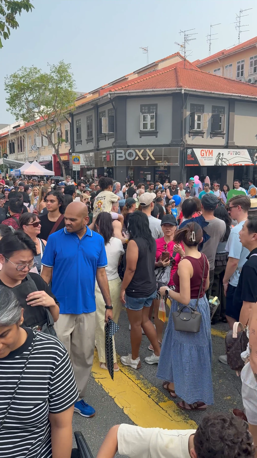 A crowd on Joo Chiat Road below the FiiTBOXX sign on a corner building.