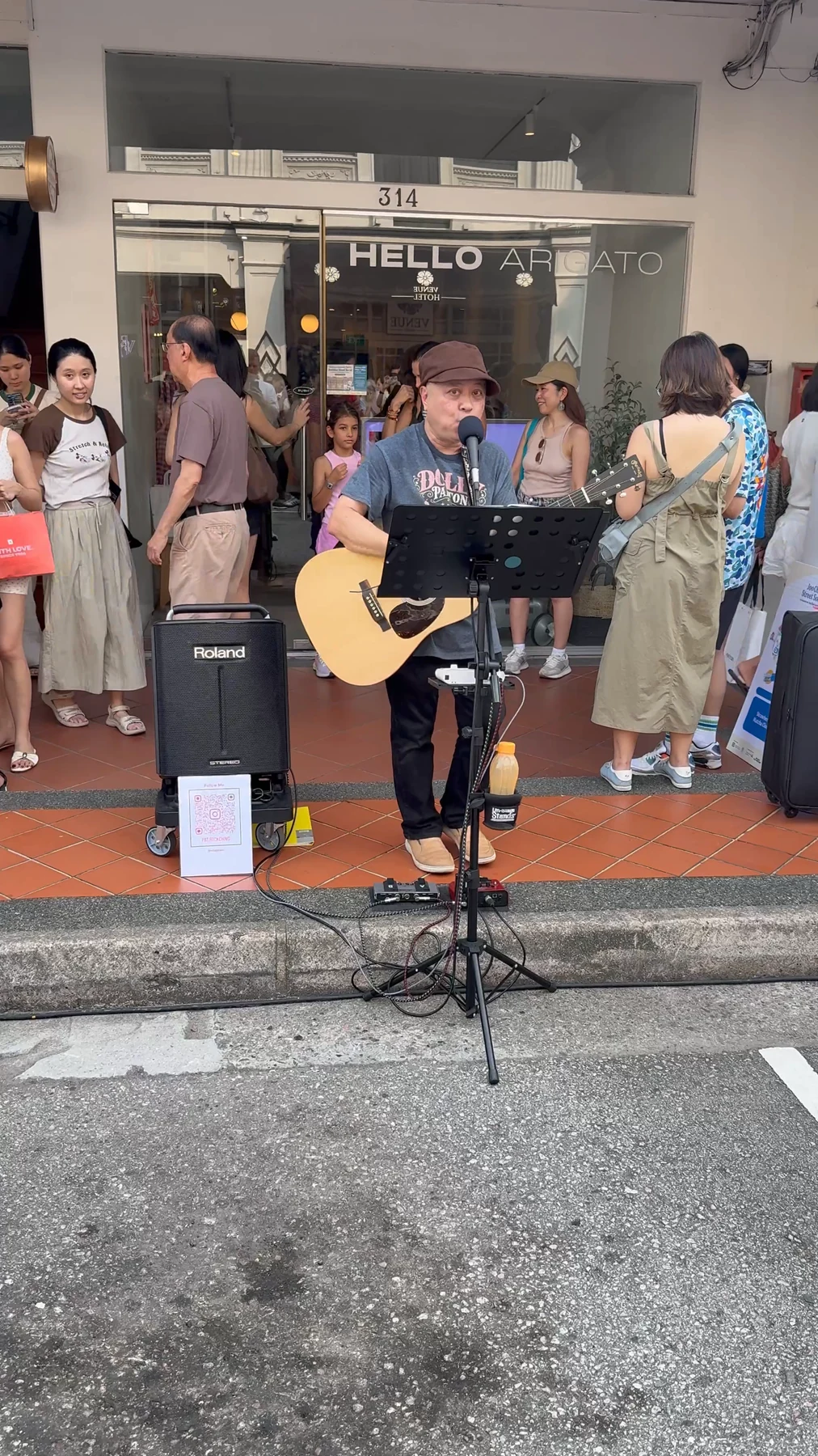 A musician sings and plays an acoustic guitar outside Hello Arigato.