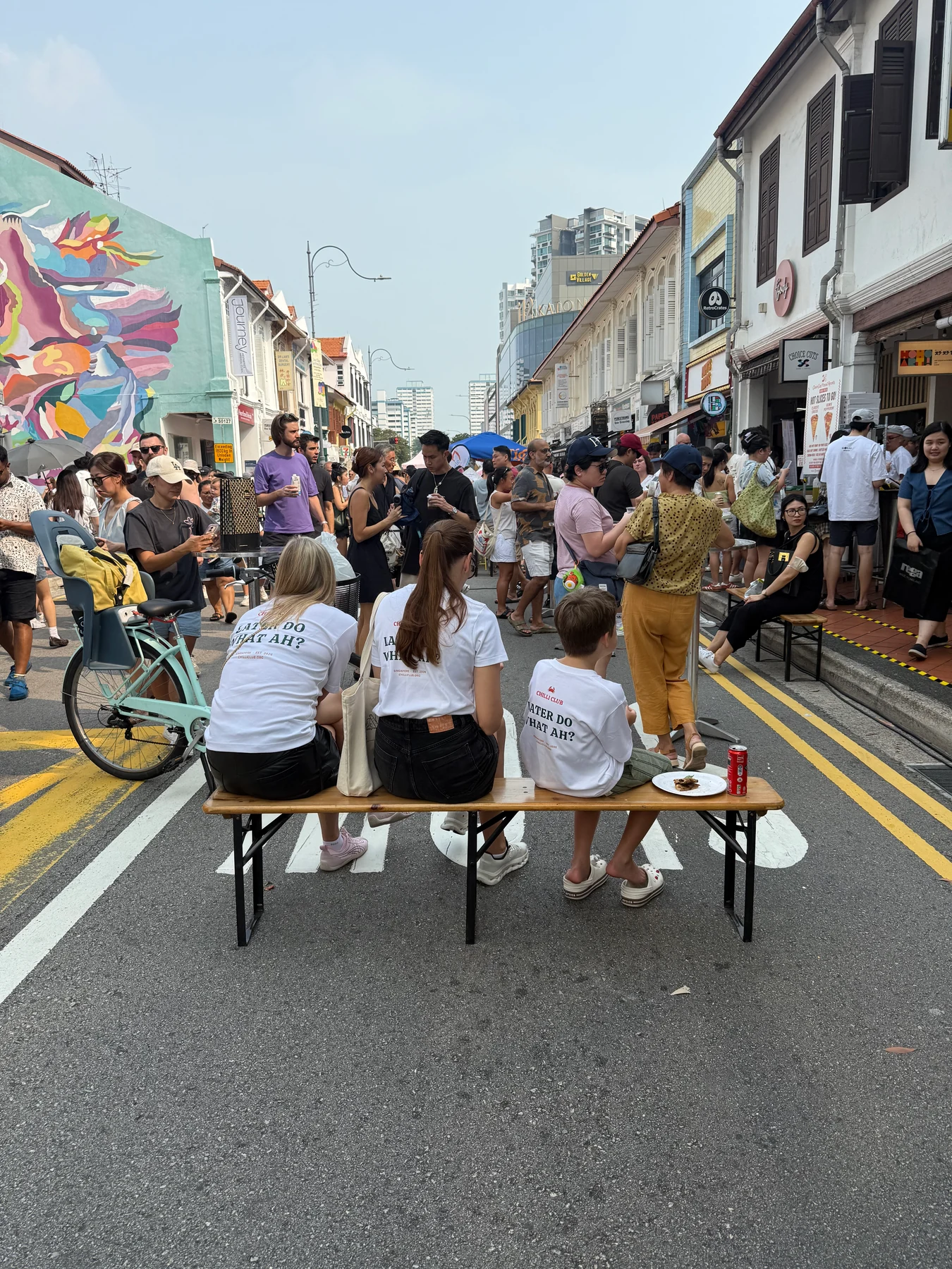 Three visitors sit with their backs to the camera, eating pizza at a table in the street.