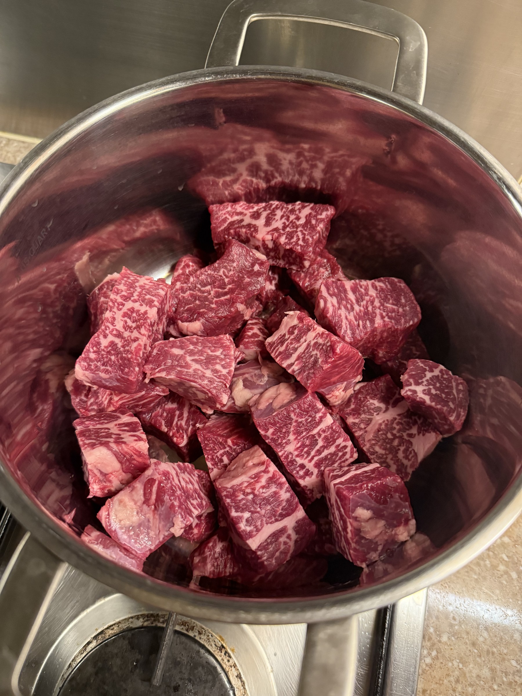 Marbled beef cut into chunks in a steel pot before marinating.